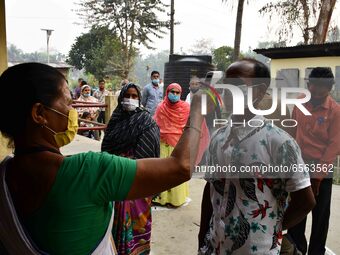 A health worker checks the body temperature of a voter, as a preventive measure against the COVID-19 coronavirus, before casting her ballot...