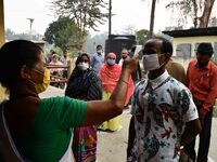 A health worker checks the body temperature of a voter, as a preventive measure against the COVID-19 coronavirus, before casting her ballot...