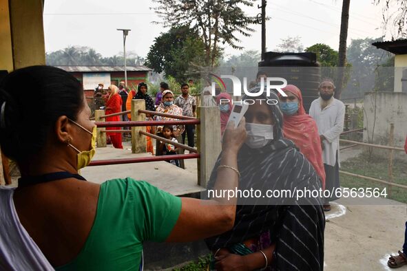 A health worker checks the body temperature of a voter, as a preventive measure against the COVID-19 coronavirus, before casting her ballot...