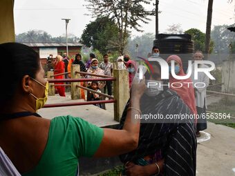 A health worker checks the body temperature of a voter, as a preventive measure against the COVID-19 coronavirus, before casting her ballot...