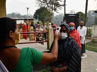 A health worker checks the body temperature of a voter, as a preventive measure against the COVID-19 coronavirus, before casting her ballot...