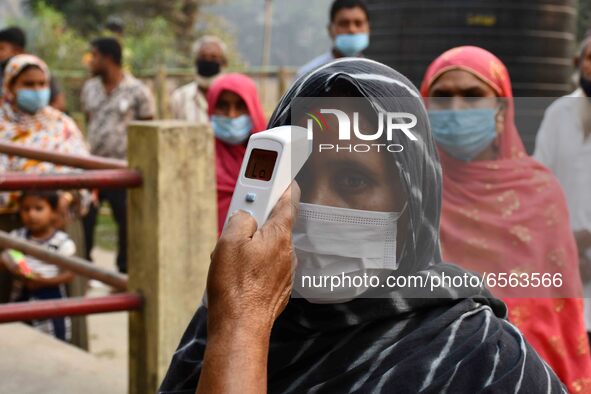 A health worker checks the body temperature of a voter, as a preventive measure against the COVID-19 coronavirus, before casting her ballot...