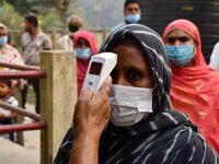 A health worker checks the body temperature of a voter, as a preventive measure against the COVID-19 coronavirus, before casting her ballot...