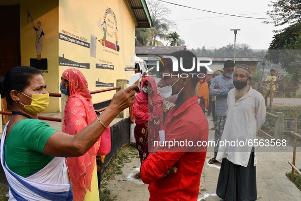 A health worker checks the body temperature of a voter, as a preventive measure against the COVID-19 coronavirus, before casting her ballot...