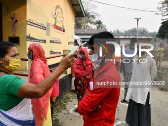 A health worker checks the body temperature of a voter, as a preventive measure against the COVID-19 coronavirus, before casting her ballot...