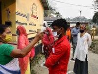 A health worker checks the body temperature of a voter, as a preventive measure against the COVID-19 coronavirus, before casting her ballot...