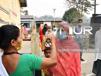 A health worker checks the body temperature of a voter, as a preventive measure against the COVID-19 coronavirus, before casting her ballot...