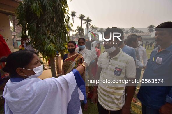 A health worker checks the body temperature of a voter, as a preventive measure against the COVID-19 coronavirus, before casting her ballot...