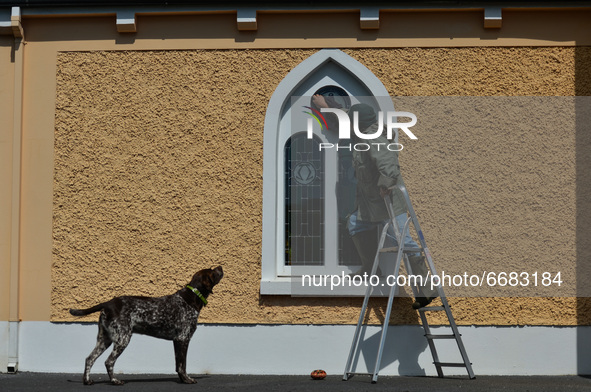 Father Krzysztof Sikora watched by his dog 'Rambo' cleans window of the 'Our Lady Star Of The Sea' catholic church in Roundstone, Connemara....