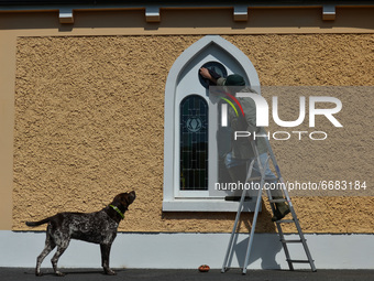 Father Krzysztof Sikora watched by his dog 'Rambo' cleans window of the 'Our Lady Star Of The Sea' catholic church in Roundstone, Connemara....