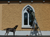 Father Krzysztof Sikora watched by his dog 'Rambo' cleans window of the 'Our Lady Star Of The Sea' catholic church in Roundstone, Connemara....