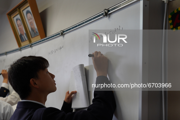 Pictures of Kim Il Sung and Kim Jong Il hang on the wall as a student solve a math quiz on a whiteboard during a math class at Hiroshima Kor...