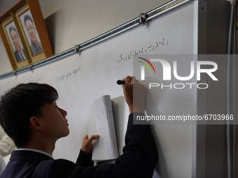 Pictures of Kim Il Sung and Kim Jong Il hang on the wall as a student solve a math quiz on a whiteboard during a math class at Hiroshima Kor...