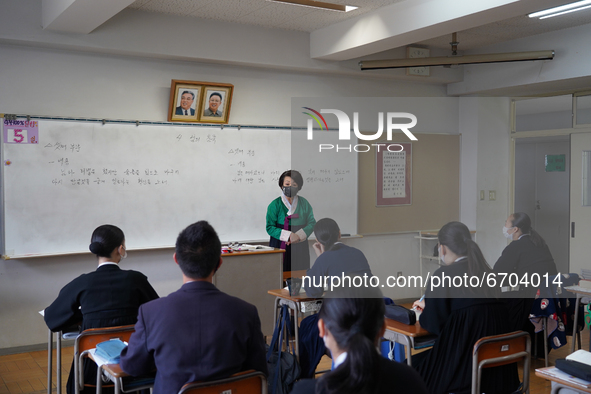 Pictures of Kim Il Sung and Kim Jong Il hang on the wall as a teacher wearing a traditional dress conducts a Korean lecture at Hiroshima Kor...