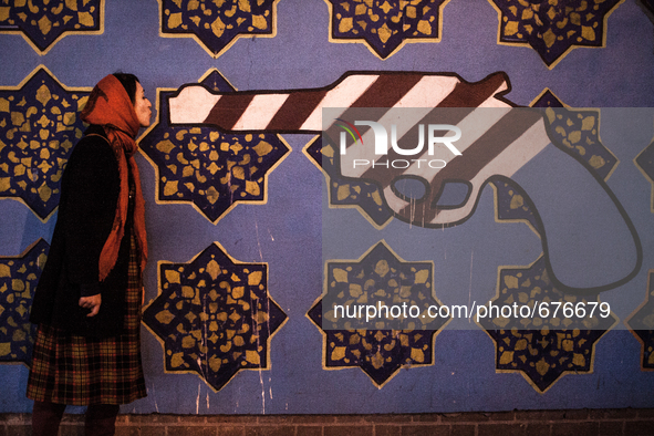 Symbolic portrait of young woman giving a kiss to a gun painted in the colors of USA on old closed US embassy in Tehran.

 