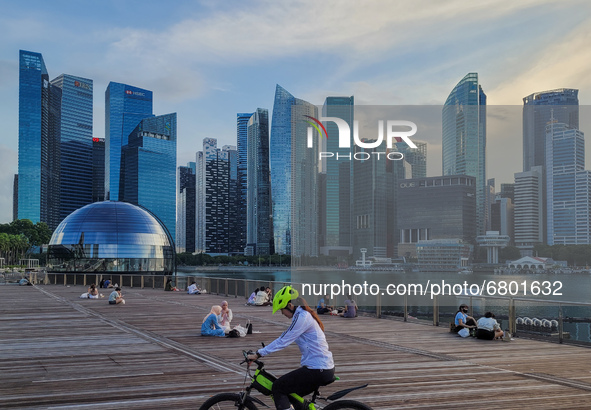 People relax on an outdoor deck as the sun sets in Marina Bay in Singapore on Monday, 14 June, 2021. Singapore begins to roll back a month o...