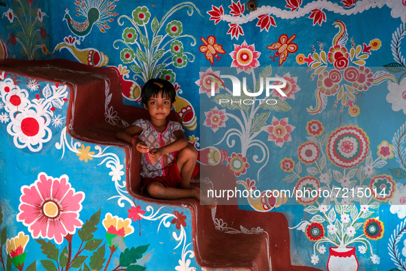 A child poses in front of a colorfully painted house in alpona village in chapainawabganj, Bangladesh. 