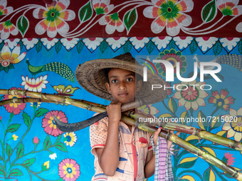 A child poses in front of a colorfully painted wall with sugarcane in alpona village in chapainawabganj, Bangladesh. (
