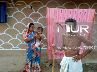 A man poses with his family in front of a painted wall in alpona village in chapainawabganj, Bangladesh (