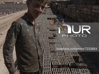 An Afghan refugee labor looks on as a young Afghan refugee boy sits on newly bricks in a brick factory, in the Borkhar area in the west of t...