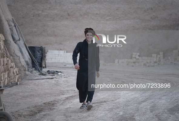 An Afghan refugee labor wearing Afghan traditional clothes smiles as he walks along an area in a brick factory after a working day in the Bo...