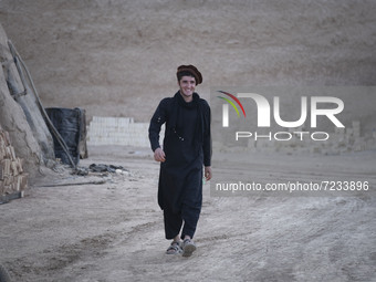 An Afghan refugee labor wearing Afghan traditional clothes smiles as he walks along an area in a brick factory after a working day in the Bo...