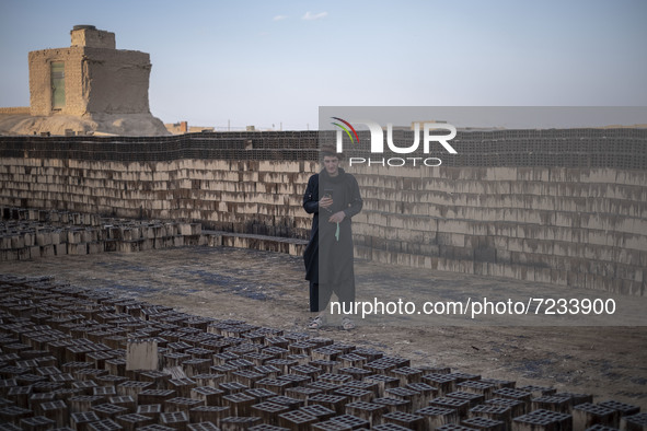 An Afghan refugee labor wearing Afghan traditional clothes uses his smartphone for a video call with his friend while standing next to the n...