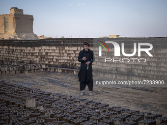 An Afghan refugee labor wearing Afghan traditional clothes uses his smartphone for a video call with his friend while standing next to the n...