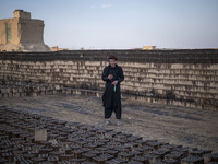 An Afghan refugee labor wearing Afghan traditional clothes uses his smartphone for a video call with his friend while standing next to the n...