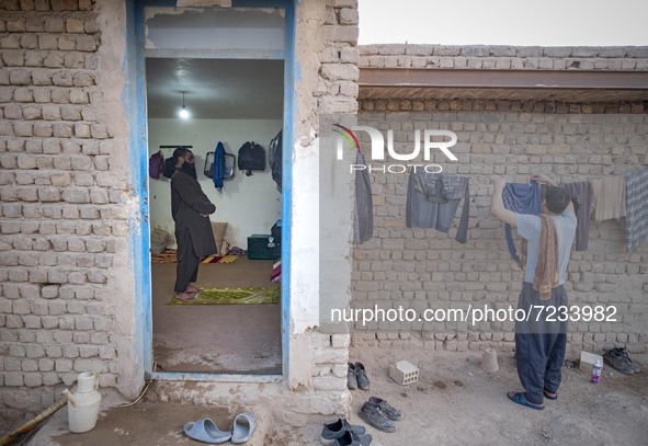 A Sunni-Afghan refugee labor prays as his colleague hangs his washed clothes from a rope out of a hut which is shared with six Afghan labore...