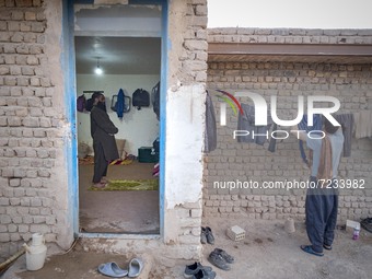 A Sunni-Afghan refugee labor prays as his colleague hangs his washed clothes from a rope out of a hut which is shared with six Afghan labore...