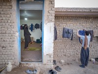 A Sunni-Afghan refugee labor prays as his colleague hangs his washed clothes from a rope out of a hut which is shared with six Afghan labore...