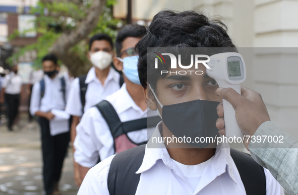 A staff checks the body temperature of a student at the entrance of School and maintain social distancing and covid protocol at the first da...