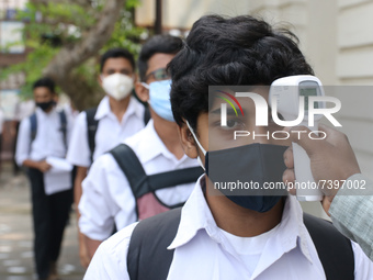 A staff checks the body temperature of a student at the entrance of School and maintain social distancing and covid protocol at the first da...