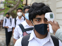 A staff checks the body temperature of a student at the entrance of School and maintain social distancing and covid protocol at the first da...