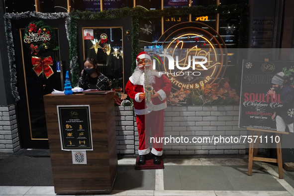 A woman talks on phone as she stands next to a Santa Claus installed outside a restaurant on the eve of Christmas, amidst the coronavirus (C...