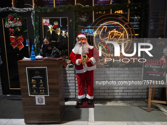 A woman talks on phone as she stands next to a Santa Claus installed outside a restaurant on the eve of Christmas, amidst the coronavirus (C...