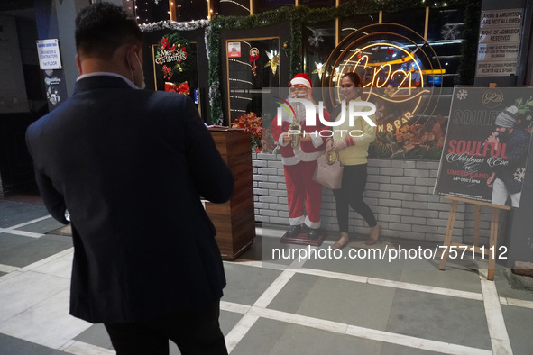 People click pictures next to a Santa Claus installed outside a restaurant on the eve of Christmas, amidst the coronavirus (COVID-19) pandem...