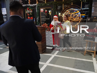 People click pictures next to a Santa Claus installed outside a restaurant on the eve of Christmas, amidst the coronavirus (COVID-19) pandem...