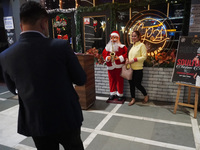 People click pictures next to a Santa Claus installed outside a restaurant on the eve of Christmas, amidst the coronavirus (COVID-19) pandem...