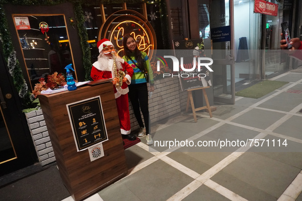 People click pictures next to a Santa Claus installed outside a restaurant on the eve of Christmas, amidst the coronavirus (COVID-19) pandem...