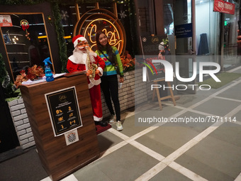 People click pictures next to a Santa Claus installed outside a restaurant on the eve of Christmas, amidst the coronavirus (COVID-19) pandem...