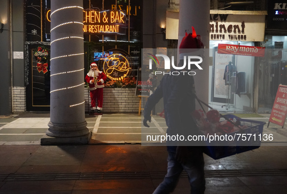 A vendor selling decorative items walks past a Santa Claus installed outside a restaurant on the eve of Christmas, amidst the coronavirus (C...