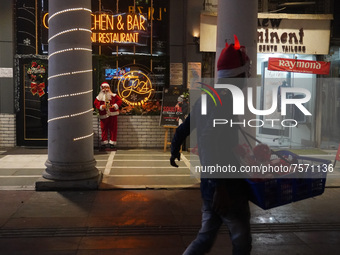 A vendor selling decorative items walks past a Santa Claus installed outside a restaurant on the eve of Christmas, amidst the coronavirus (C...