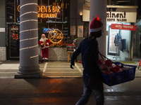 A vendor selling decorative items walks past a Santa Claus installed outside a restaurant on the eve of Christmas, amidst the coronavirus (C...