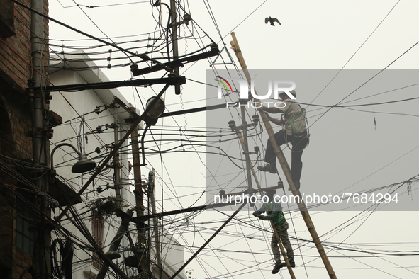 A worker hangs from an electric post while he repairs power lines in Kolkata on January 24,2022. 