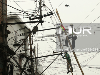 A worker hangs from an electric post while he repairs power lines in Kolkata on January 24,2022. (