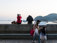 A mother and her daughter pass on Stanley promenade as a couple enjoys the sunset in Hong Kong, China, on February 27, 2022. (