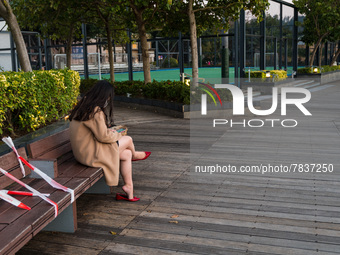 A young lady and her dog sits on a bench wrapped with red tape in Hong Kong, China, on February 27, 2022. (