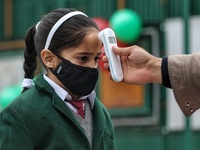 An employee checks the temperature of a student at the entrance of Baramulla public school in Baramulla Jammu and Kashmir India on 02 March...